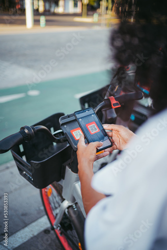 Perspective shot of a woman scanning a qr code with phone to rent an electric bike in the city.