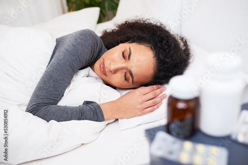 Fotografia A young multi-ethnic woman sleeps in bed recovering from flu with medication