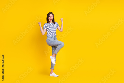 Full size photo of satisfied lady raise arm leg rejoice black friday sale good shopping empty space isolated on yellow color background
