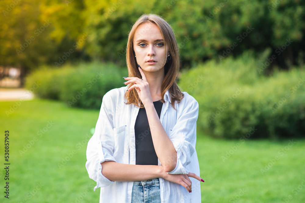 Portrait of a young and attractive Caucasian girl in casual clothes in a park in nature on a sunny day. Portrait of a young and attractive Caucasian girl in casual clothes in a park in nature on a sunny day.