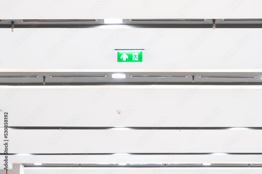 White neon sign depicting a fire exit with green background hangs from the ceiling. White neon sign depicting a fire exit with green background hangs from the ceiling.