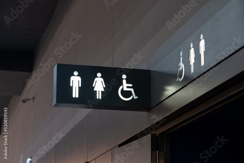 A sign of restroom lighten in white standout from a black plate. The restroom is inside a building, decorated in black and white tone.