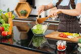 Close up hands of Asian woman wearing apron, tossing the vegetarian salad with wooden spatulas. Preparing a healthy salad with fresh vegetables such as carrot, tomato cabbage and green oak.