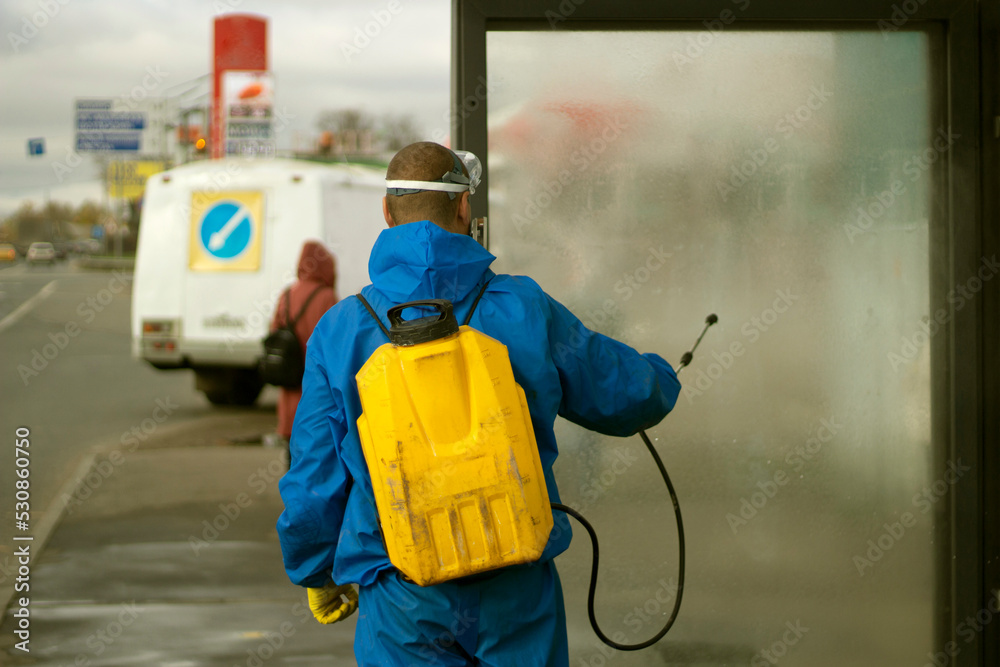 Guy washes bus stop. Worker with canister of water. Spraying detergent on glass.