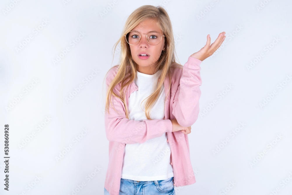 Studio shot of frustrated caucasian blonde little girl wearing pink jacket and glasses over white background gesturing with raised palm, frowning, being displeased and confused with dumb question. Studio shot of frustrated caucasian blonde little girl wearing pink jacket and glasses over white background gesturing with raised palm, frowning, being displeased and confused with dumb question.