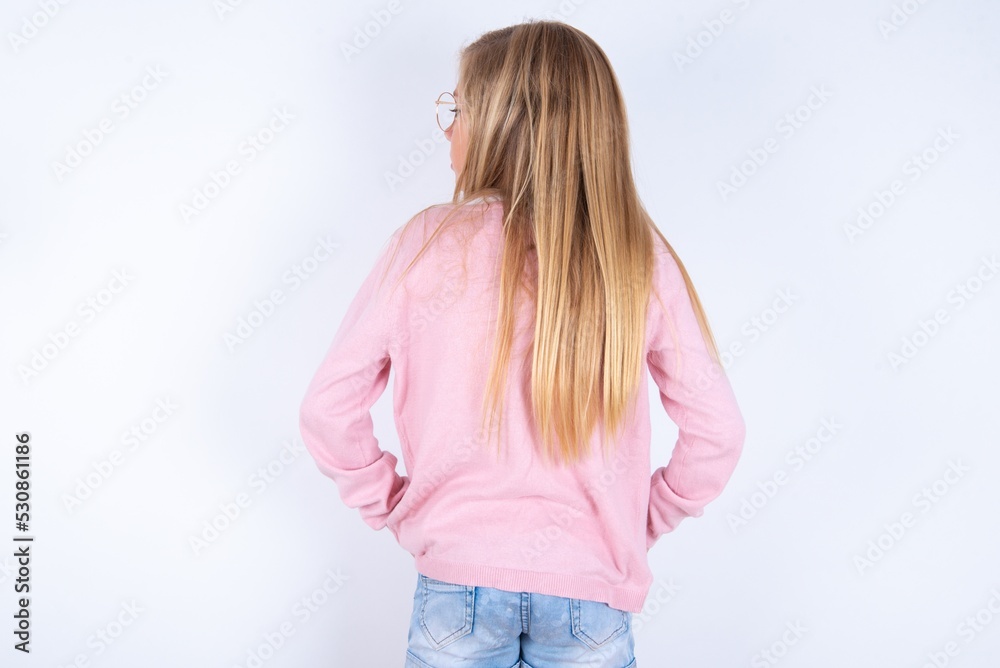 The back view of caucasian blonde little girl wearing pink jacket and glasses over white background Studio Shoot. The back view of caucasian blonde little girl wearing pink jacket and glasses over white background Studio Shoot.