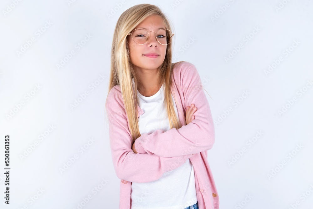 Waist up shot of self confident caucasian blonde little girl wearing pink jacket and glasses over white background has broad smile, crosses arms, happy to meet with colleagues. Waist up shot of self confident caucasian blonde little girl wearing pink jacket and glasses over white background has broad smile, crosses arms, happy to meet with colleagues.