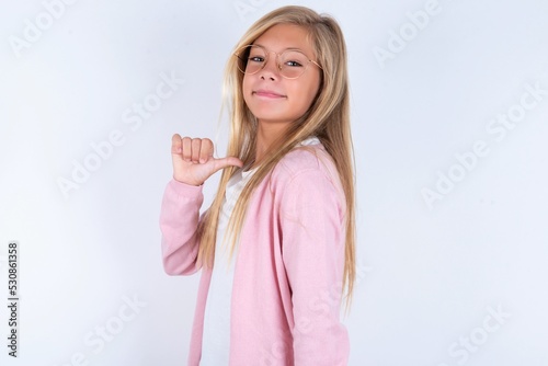 Canvas Print Closeup of cheerful caucasian blonde little girl wearing pink jacket and glasses over white background looks joyful, satisfied and confident, points at himself with thumb