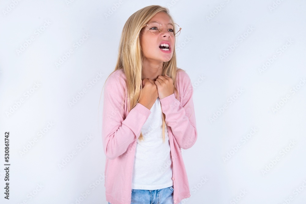 caucasian blonde little girl wearing pink jacket and glasses over white background excited and glad to achieve victory, clenches fists, screams in excitement with closed eyes,successful person. caucasian blonde little girl wearing pink jacket and glasses over white background excited and glad to achieve victory, clenches fists, screams in excitement with closed eyes,successful person.