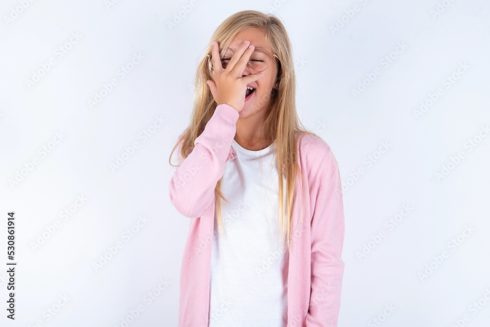 Charismatic carefree joyful caucasian blonde little girl wearing pink jacket and glasses over white wall likes laugh out loud not hiding emotions giggling hear funny hilarious joke chuckling facepalm. Charismatic carefree joyful caucasian blonde little girl wearing pink jacket and glasses over white wall likes laugh out loud not hiding emotions giggling hear funny hilarious joke chuckling facepalm.