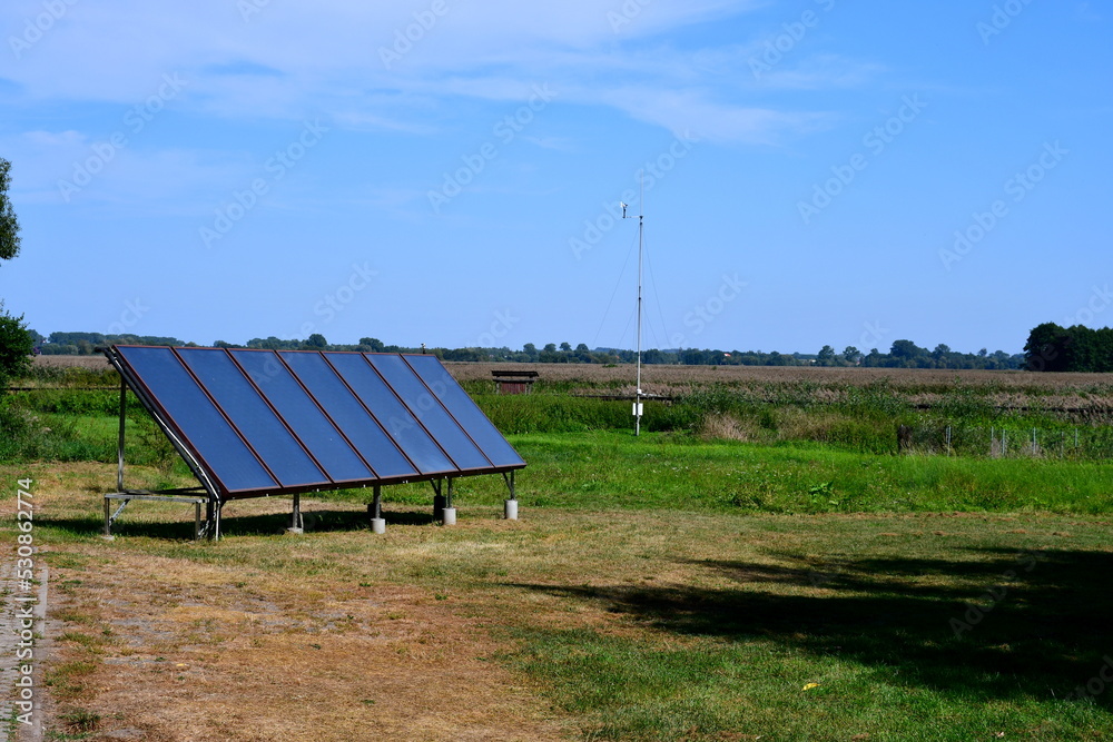 A close up on a set of solar panels used to gather and generate energy located in the middle of a vast field, meadow, or pastureland seen on a sunny summer day on a Polish countryside