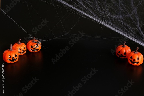 small Beautiful pumpkins and two black small spider in the web on a black background. Creative halloween concept backdrop.