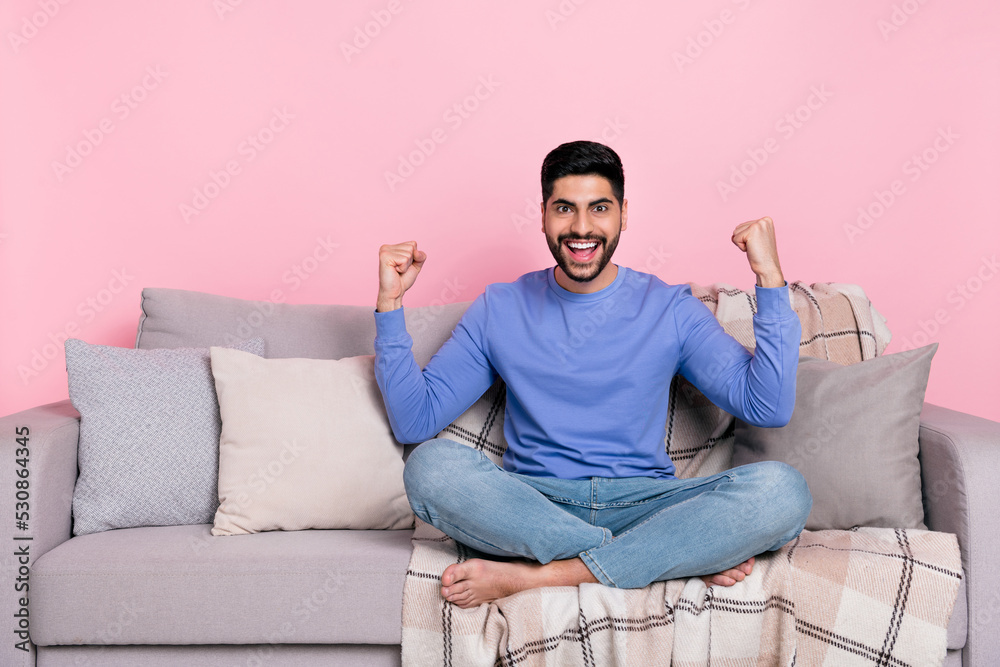 Obraz premium Photo of shiny lucky arab guy dressed blue pullover sitting couch rising fists isolated pink color background