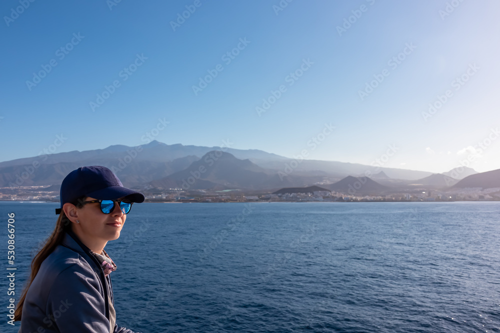 Woman enjoying the panoramic view from a ferry on the landscape around volcano mount Pico del Teide, Canary Islands, Spain, Europe. Boat is connecting Tenerife and La Gomera. Island hopping vacation