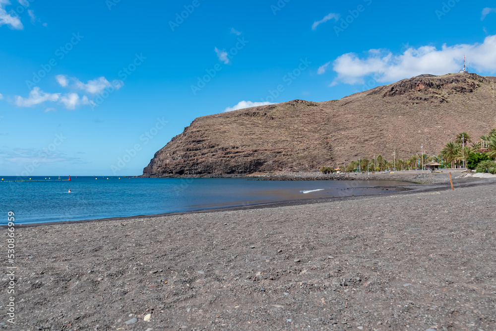 Fototapeta premium Panoramic view from the beach Playa de San Sebastian on Cruz de Machal in San Sebastian de La Gomera, La Gomera, Canary Islands, Spain, Europe. Dark lava sand beach. Mountains in the back