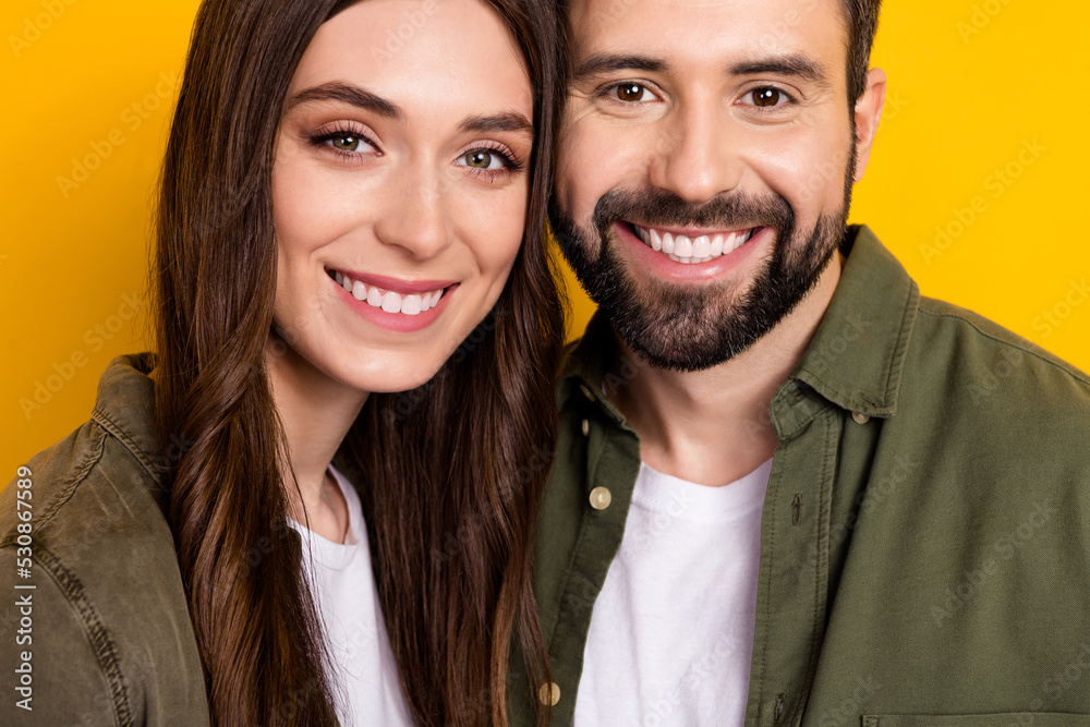 Cropped portrait of two cheerful peaceful people toothy smile look camera isolated on yellow color background Cropped portrait of two cheerful peaceful people toothy smile look camera isolated on yellow color background