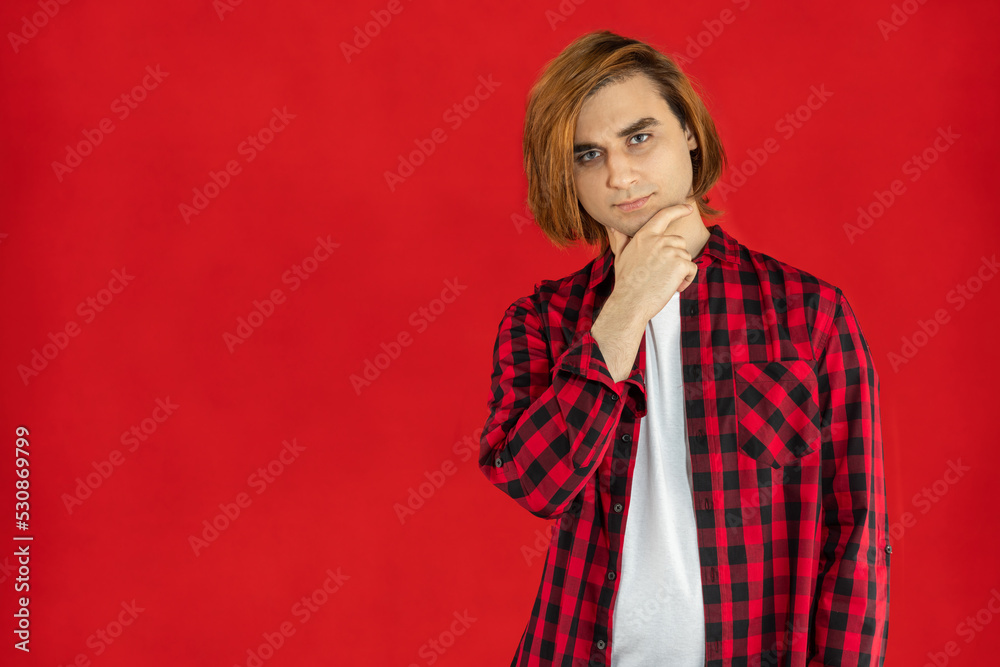 Young man Prep Student with long hair. Portrait of a guy with hand on chin. Red background Young man Prep Student with long hair. Portrait of a guy with hand on chin. Red background