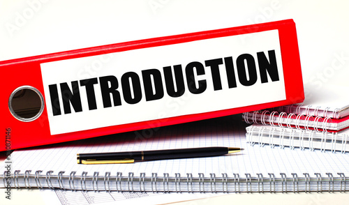 On the desktop are notebooks, a pen and a red folder for papers with the text INTRODUCTION. Business concept
