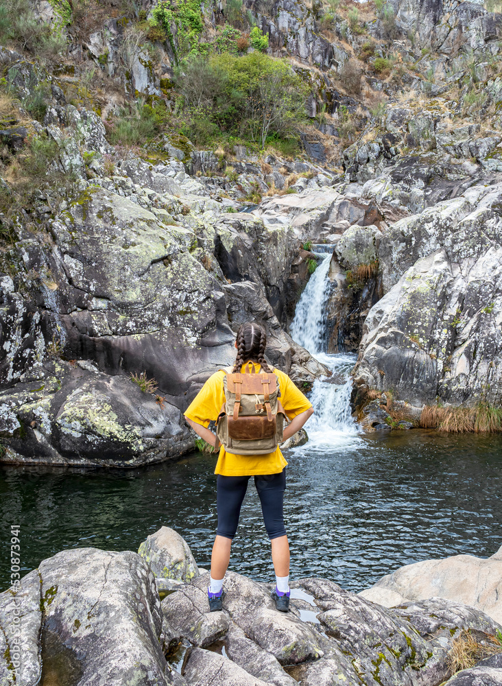 Girl with arms on hips looking at a waterfall.