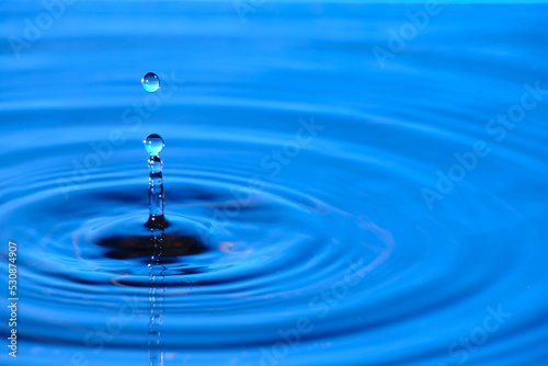 Splash drop of water with diverging water circles, on blue background.