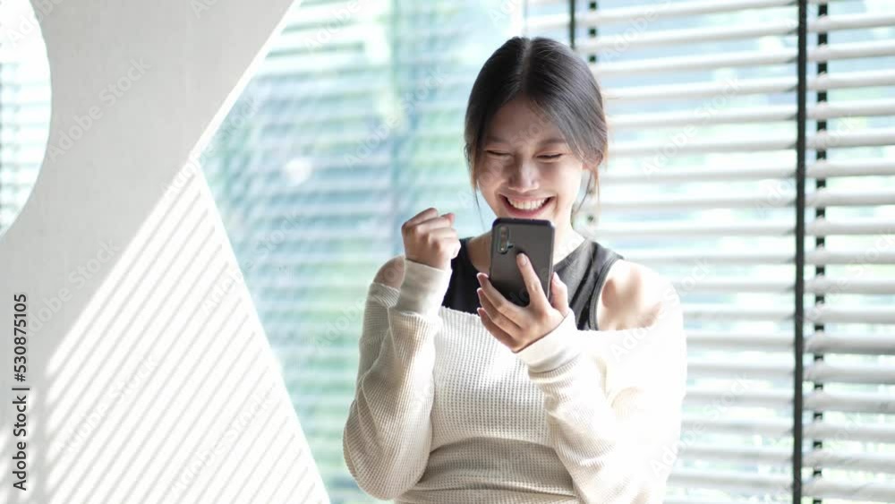 Happy and excited Asian woman holding a smartphone and winning