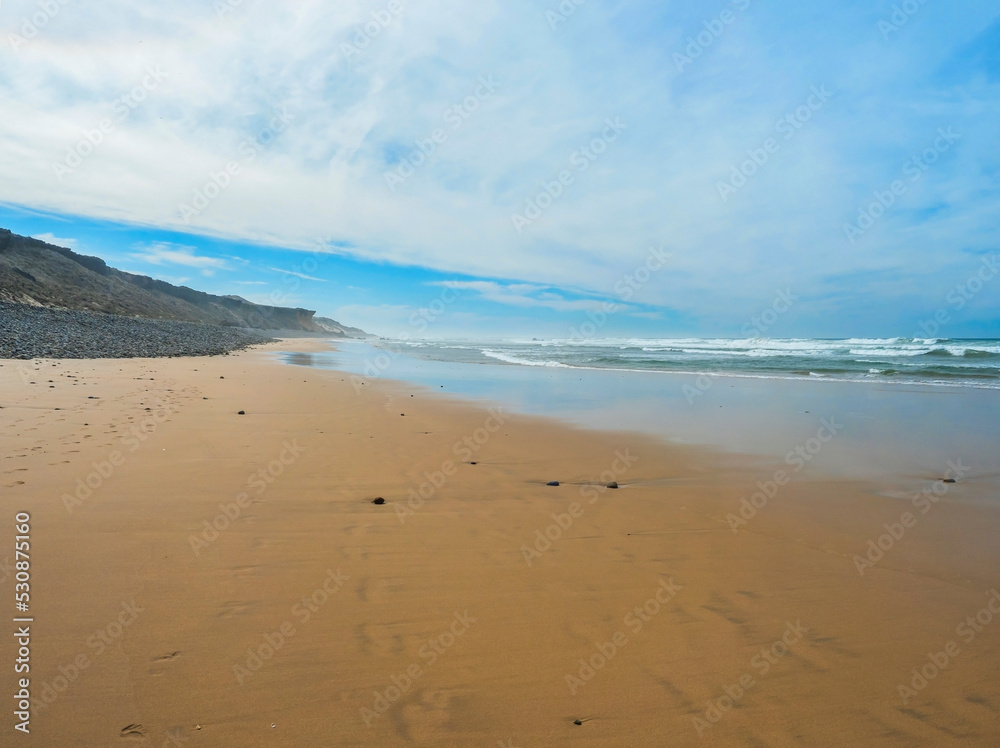 View of empty Praia do Queimado beach with ocean waves and sharp rocks and wet golden sand at wild Rota Vicentina coast near Porto Covo, Portugal. View of empty Praia do Queimado beach with ocean waves and sharp rocks and wet golden sand at wild Rota Vicentina coast near Porto Covo, Portugal.