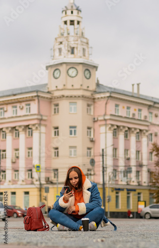 Beautiful young woman sitting outside on street together with cell phone Outdoors city background. Lifestyle