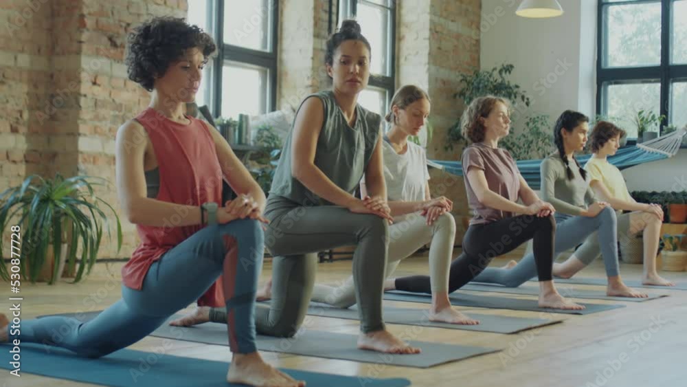 Female fitness instructor and group of women doing lunge and runner stretch during yoga workout in studio