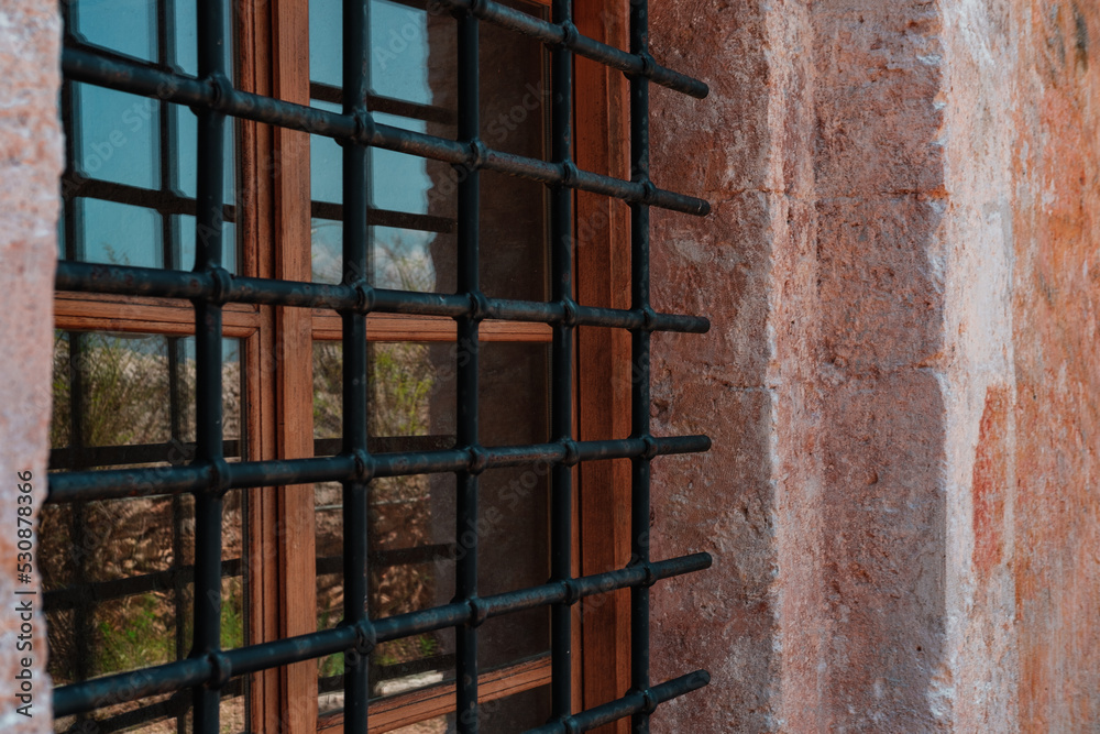 window with iron protection of the ancient stone building, medieval architecture details, old european fortress window with iron protection of the ancient stone building, medieval architecture details, old european fortress