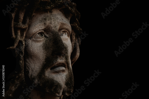 Antique stone statue Jesus Christ in a crown of thorns aagainst black background. Copy space.