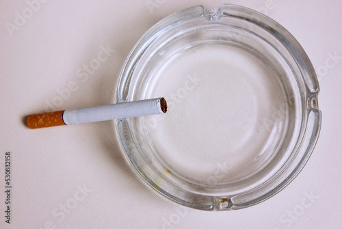 cigarette and an ashtray on white background. the cigarette is on the ashtray. Yellow filter. Harm to health. It a bad habit. The vision of world without tobacco, tobacco and lung health. Lung cancer.