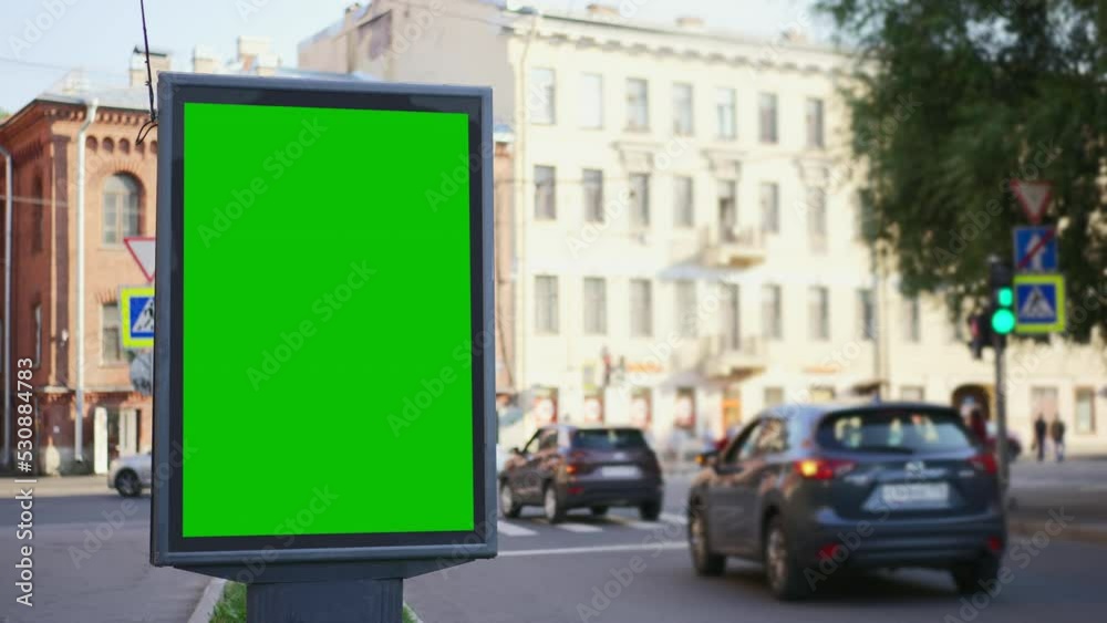 4k Green mockup billboard and cars drive in city street spbd. Vertical digital screen for advertising standing in center of modern town and transport moving on road in summer day. View of beautiful