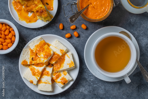 Slices of adyghe cheese poured over sea buckthorn jam with green tea and fresh raw sea buckthorn berries. Healthy breakfast concept photo