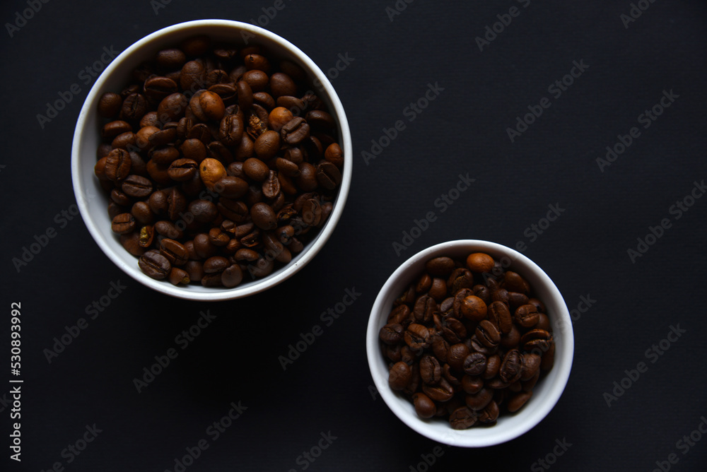 Delicious coffee beans in a ceramic white bowl on a black background. Coffee beans close-up in the dishes. Delicious coffee beans in a ceramic white bowl on a black background. Coffee beans close-up in the dishes.