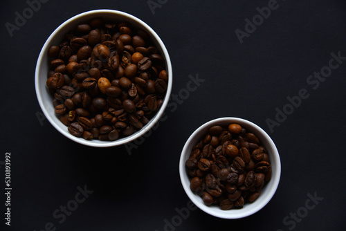 Delicious coffee beans in a ceramic white bowl on a black background. Coffee beans close-up in the dishes.