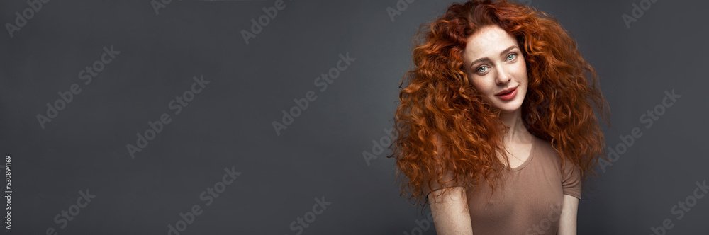 Fototapeta premium Banner. Portrait of a red-haired woman on a dark gray background. The woman looks directly into the camera. With space to copy. High quality photo