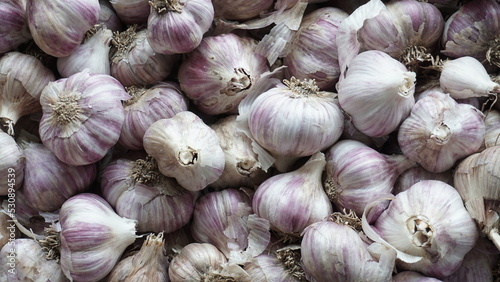 
A large amount of garlic in a chaotic arrangement. Garlic is gray in color, large and small in the outer husk