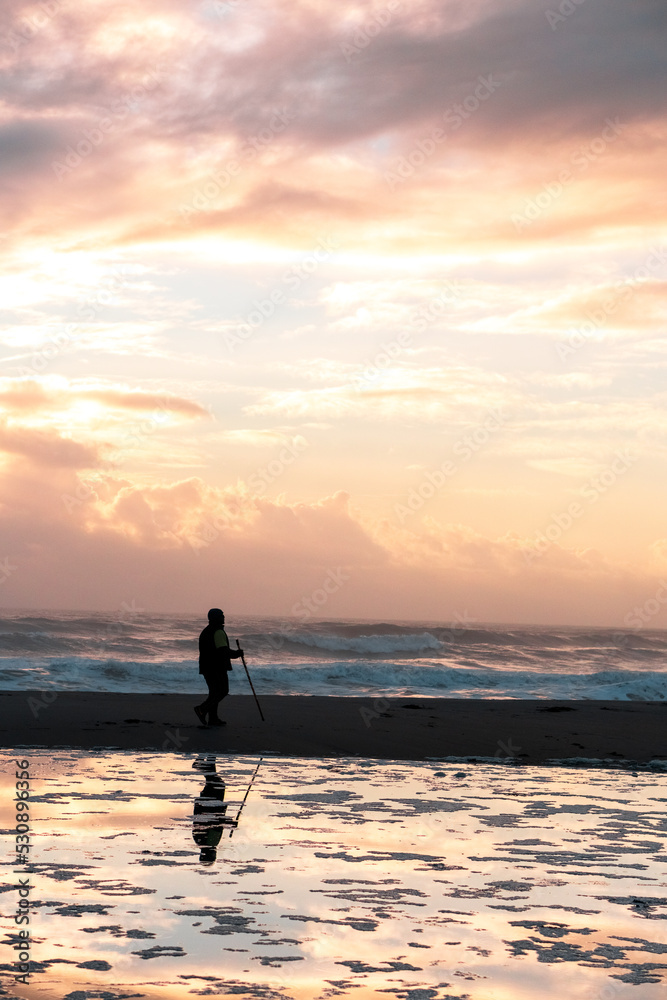 Silhouetted man walking down the beach during sunrise