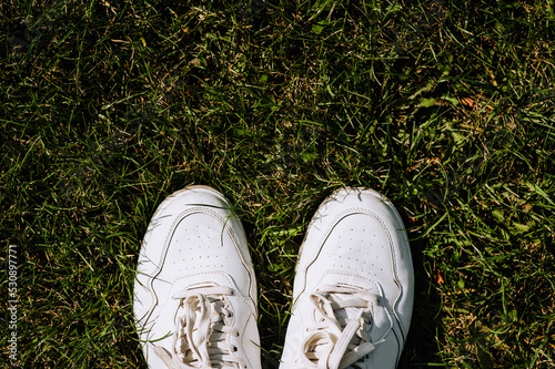 A man in white leather sneakers stands on the green grass of a meadow.