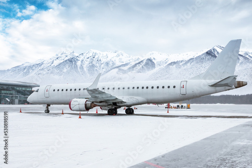 White passenger jetliner on the airport apron against the backdrop of snow-capped mountains © Dushlik