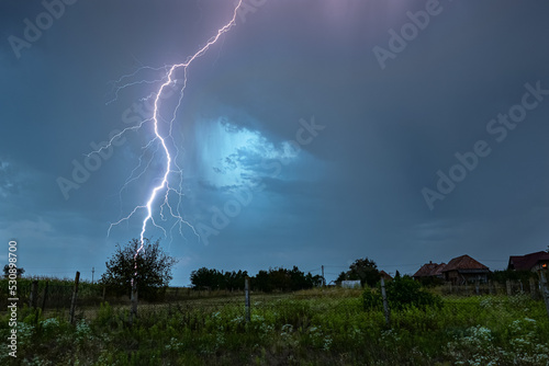 Powerful branched thunderbolt of lightning strikes down in an idyllic countryside