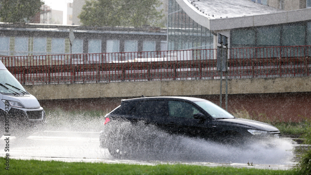 Samochód w czasie opadów deszczu jedzie ulicą miasta.  - obrazy, fototapety, plakaty 
