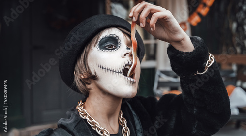 Fotografie Beautiful scary little girl celebrating halloween, chewing gummy worm