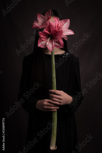 studio art portrait of woman in black dress holding pink amaryllis flower hiding her face photo
