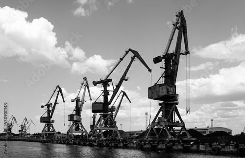Harbor pier with many cranes and stacks of bulk cargo, coal and wood chips, black and white photo