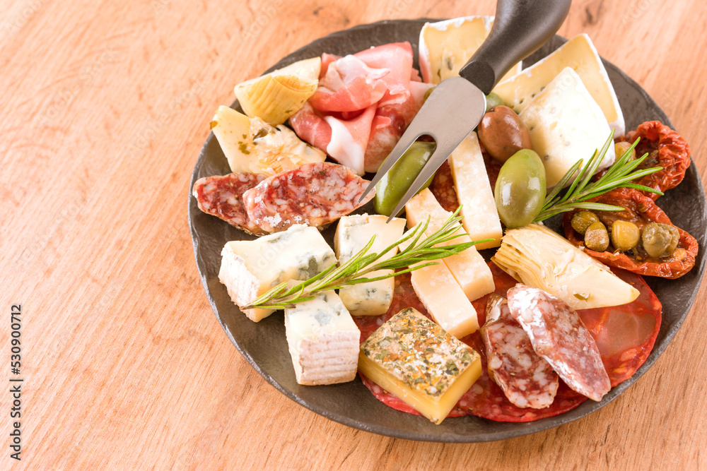 Italian antipasti plate with variety of cheeses, sausages served with sun dried tomatoes, olives and herbs on wooden table. Cheese and meat snacks platter. Menu background