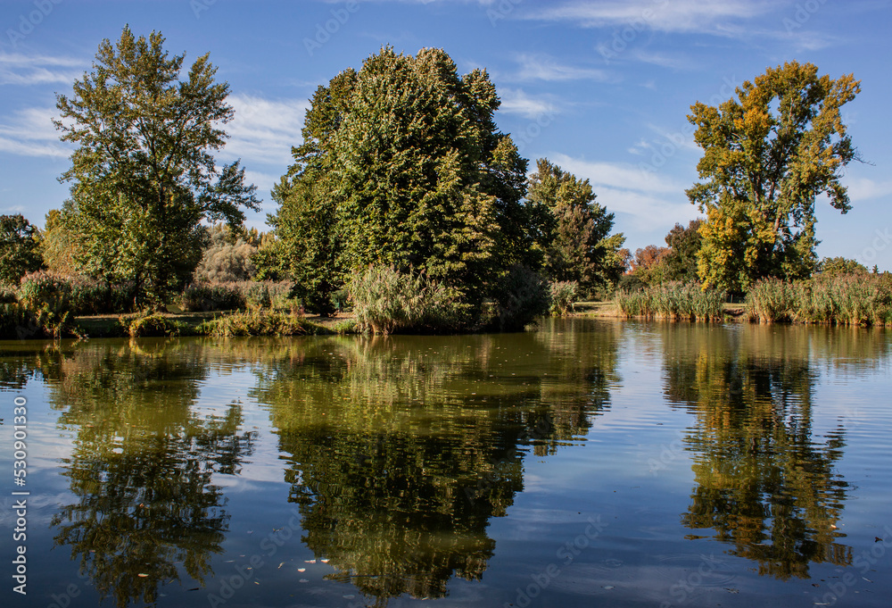 A beautiful boating lake and colorful trees and their reflection in Sárvár, West Hungary, Europe. Sustainable industry, ecosystem, and healthy environment concepts and background. A beautiful boating lake and colorful trees and their reflection in Sárvár, West Hungary, Europe. Sustainable industry, ecosystem, and healthy environment concepts and background.