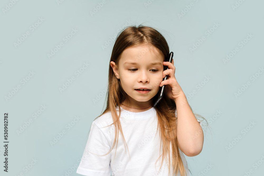 Cute caucasian baby girl talking on the phone, isolated in studio with blue background, little girl listening to news from mom Cute caucasian baby girl talking on the phone, isolated in studio with blue background, little girl listening to news from mom