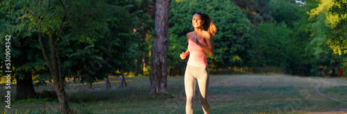 Young smiling fitness woman running in park in summer