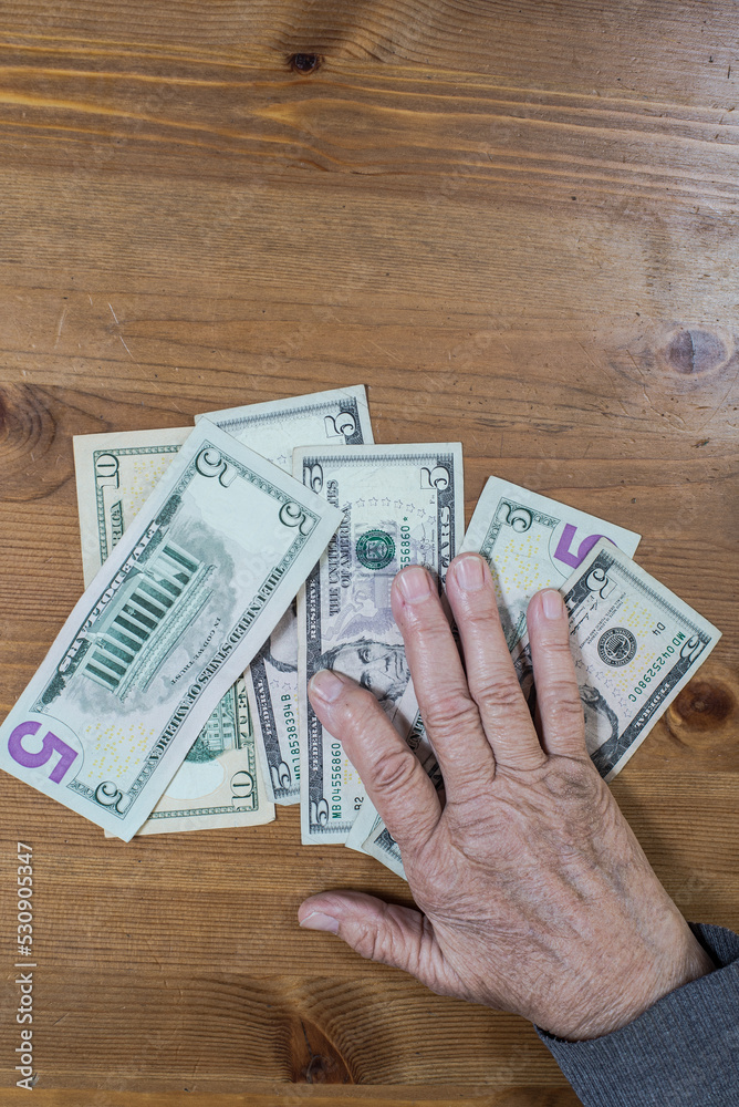 hands of an old woman lie on dollar bills on the table. View from above. hands of an old woman lie on dollar bills on the table. View from above.